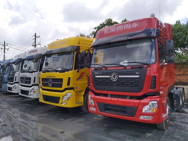 A row of large commercial trucks in various colors parked side-by-side in an outdoor lot.