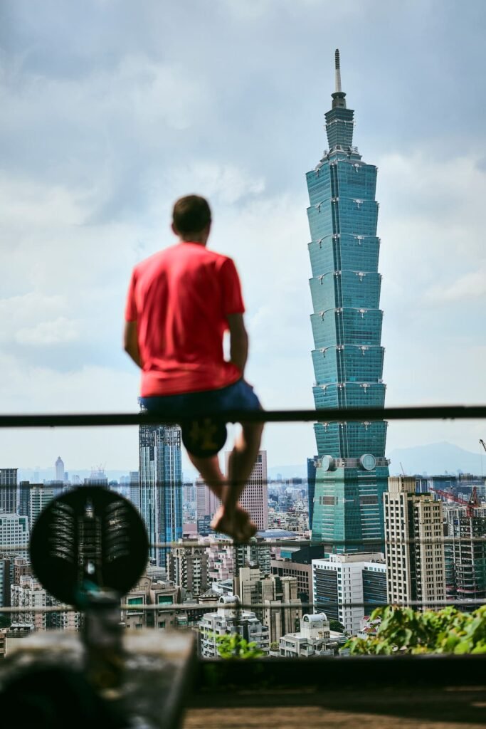 Alex Honnold overlooking Taipei city, facing the distant Taipei 101 skyscraper.